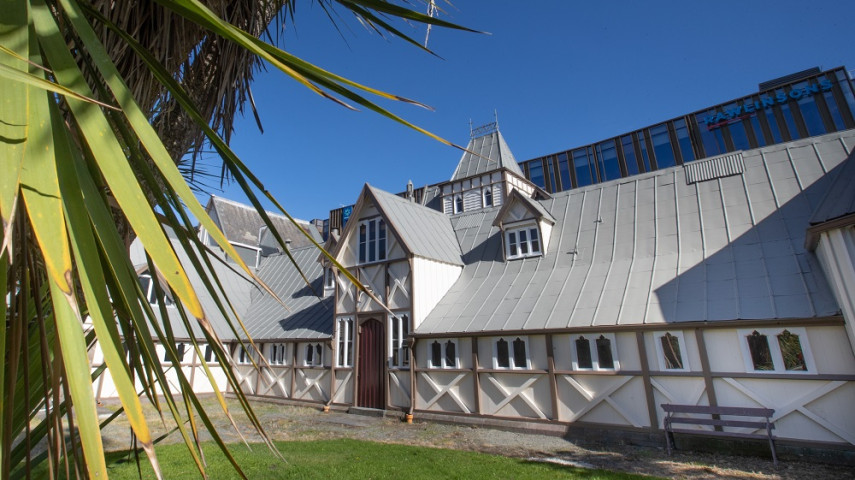 Old building with a grey metal roof and timber-style walls, with a palm tree in the foreground.
