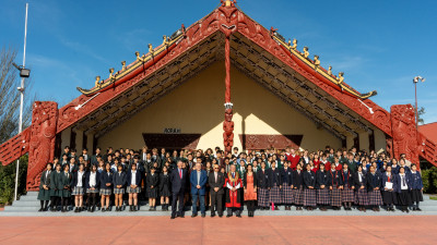 A group of students in school uniforms stand in front of a marae during a special mayoral welcome.